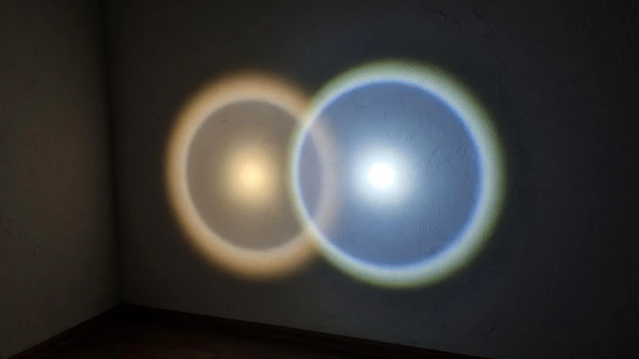 Two overlapping flashlight beams on a dark wall, one warm white and one cool white with a brighter center.